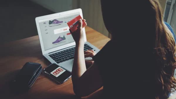 A woman shops online using a laptop and credit card on a wooden table.