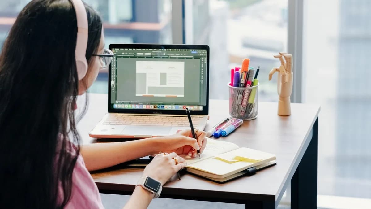 Woman using laptop and notebook in modern home office setup, enhancing productivity.