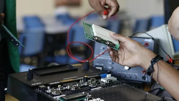 Close-up of hands working with electronics equipment and circuit board in a lab setting.