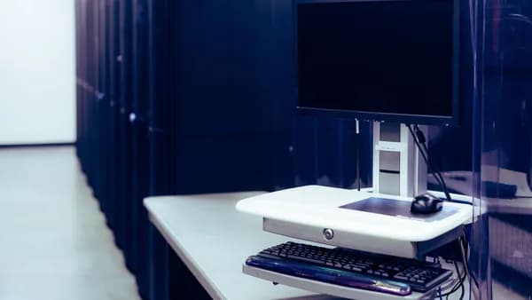 Contemporary computer with black screen placed on stand near row of server steel racks in data center