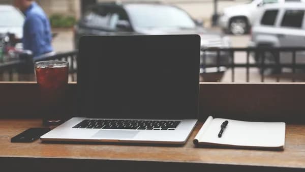 MacBook Pro on a wooden table with iced coffee and notebook in a casual coffee shop setting.