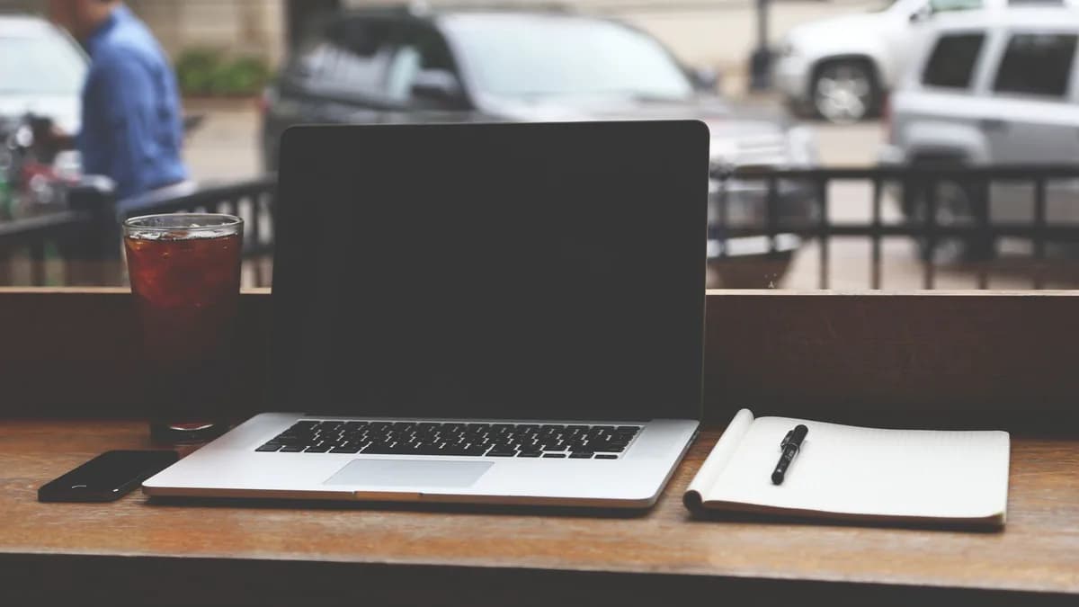 MacBook Pro on a wooden table with iced coffee and notebook in a casual coffee shop setting.