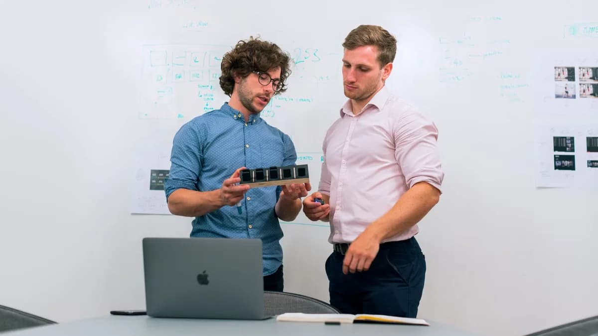 Two men in an office discussing and reviewing a tech prototype.