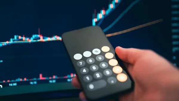 Close-up of a smartphone displaying a calculator with a financial chart in the background.
