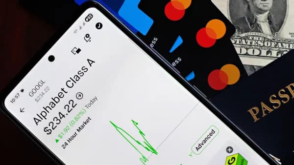 A smartphone displaying Alphabet stock price alongside credit cards, cash, and passport.