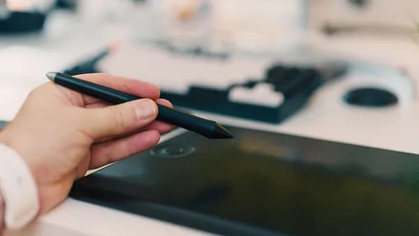 Close-up of a hand using a stylus on a digital tablet in an office setting.