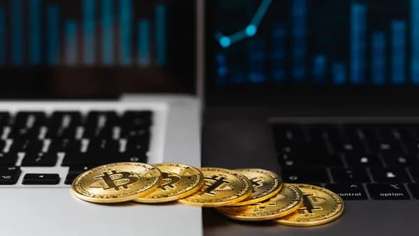 Gold bitcoins placed on laptop keyboards with digital financial graphs in the background.
