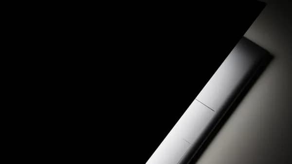 A partial view of a modern laptop closed in shadow, highlighting its sleek design.