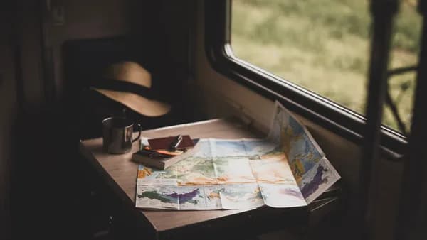 A serene train ride setup with a world map, mug, and hat on a table, suggesting travel plans.