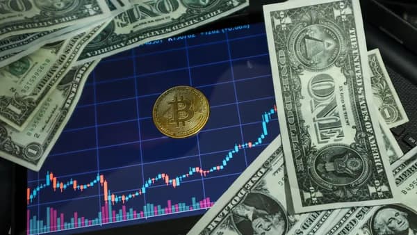 Bitcoin coin on a tablet showing stock chart, surrounded by dollar bills.