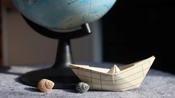 A paper boat and seashells beside a globe, symbolizing travel dreams.