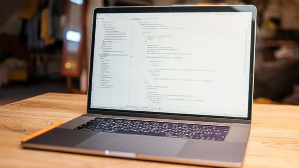 Open laptop with visible code on screen on a wooden desk in a modern, cozy workspace.