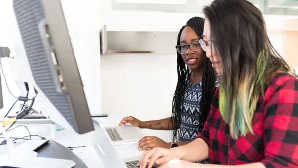 Two women working together on laptops in a bright, modern office space.