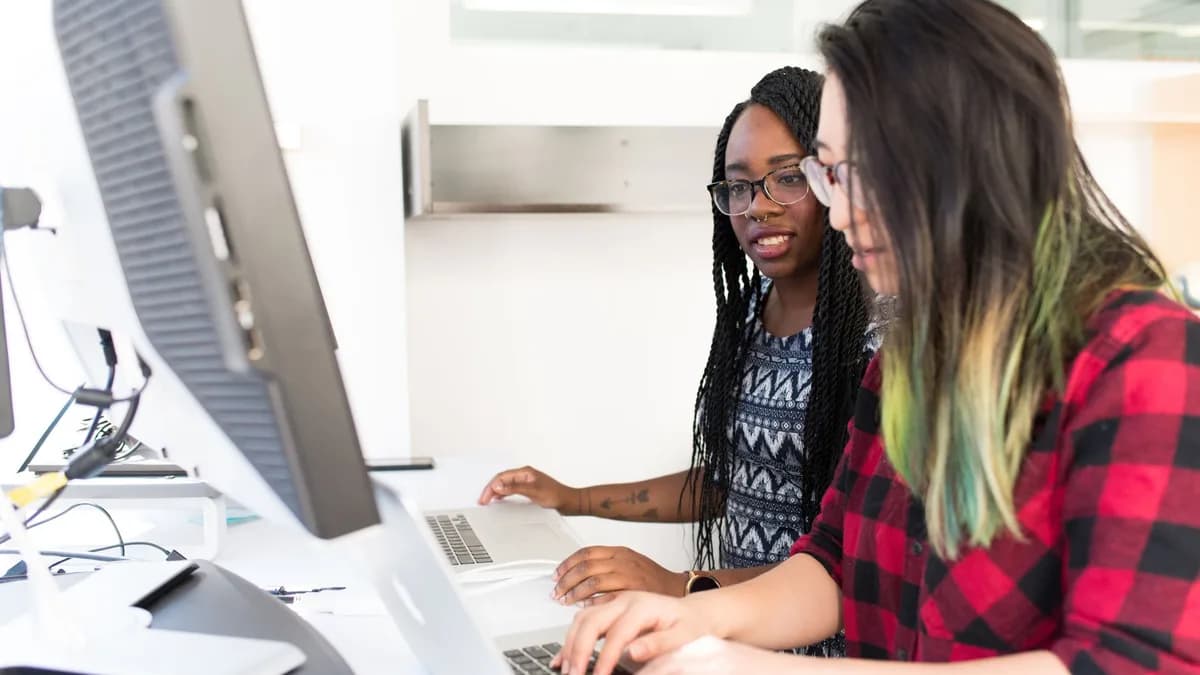 Two women working together on laptops in a bright, modern office space.
