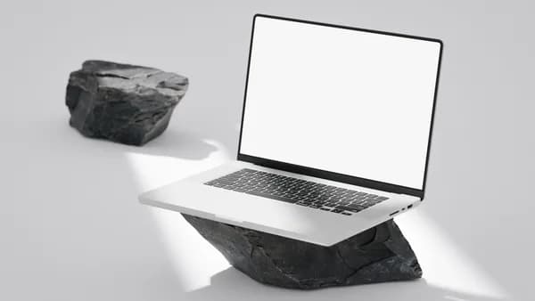Elegant laptop with blank screen balanced on rocks in a minimalist setting.