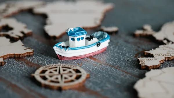 A close-up of a toy boat on a wooden map with a compass, representing travel and navigation.