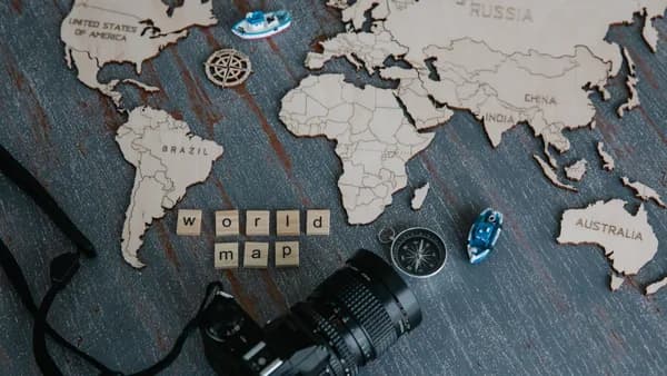 A creative flat lay of a wooden world map, camera, and compass.