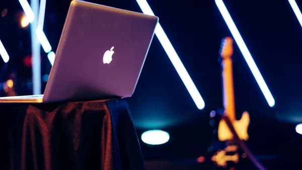 A sleek laptop sits on a table with vibrant neon lights and a guitar in the background.