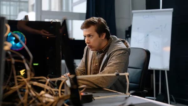 Young man intensely focused on computer work in a tech office setting with a whiteboard in the background.