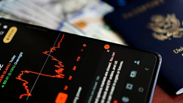 Close-up of a smartphone displaying a stock market app alongside a US passport and currency.
