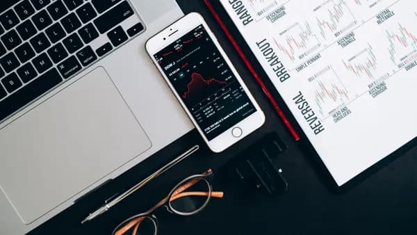 Top view of financial tools including a laptop, smartphone with stock data, and charts for market analysis.