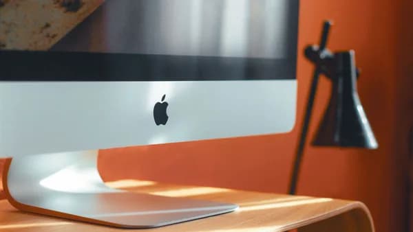 A sleek computer and stylish desk lamp on a wooden table in a modern workspace.
