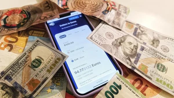 A smartphone displaying a currency converter surrounded by dollar and euro banknotes, highlighting exchange rates.