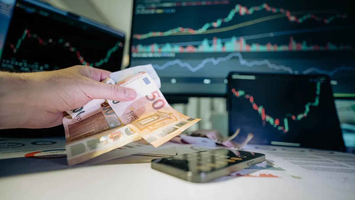 Business professional counting Euro notes with financial charts on screens, indicating investment strategy.
