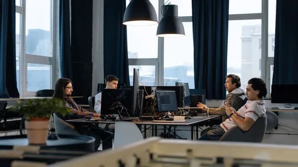 Workers collaborate in a modern office with computers, showcasing teamwork in technology development.