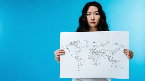 Portrait of a young woman holding a world map against a vivid blue background.