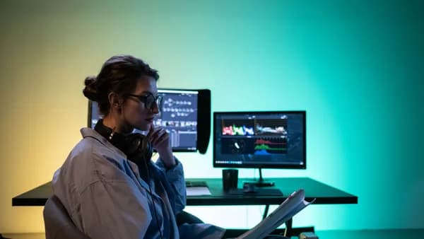 Woman editing video at modern desk setup with dual monitors in an office.