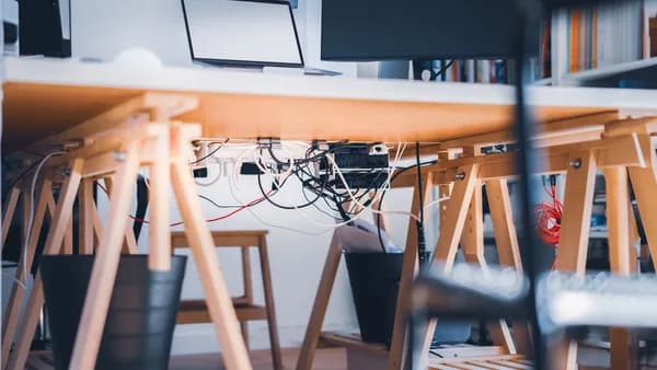 A stylish workspace with visible cables, laptop and monitor, highlighting modern technology's complexity.