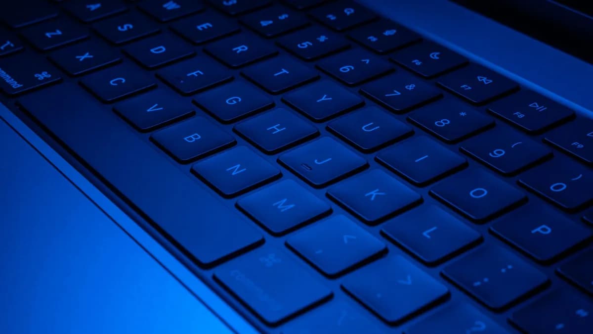 Close-up image of a laptop keyboard illuminated with blue light, showcasing modern technology design.