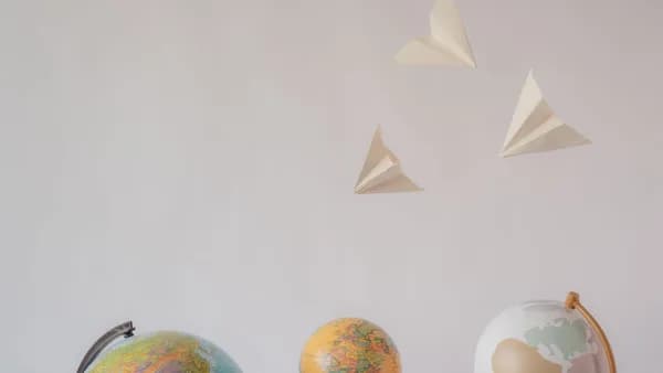 Paper airplanes fly over colorful globes, symbolizing travel and exploration on a white background.