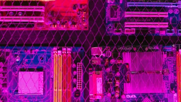 Colorful circuit boards behind a wire mesh, enhanced with pink and purple hues.