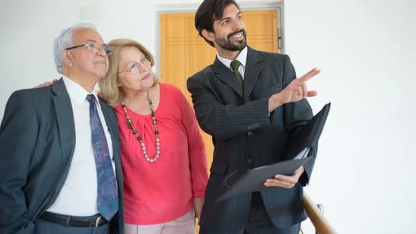 An elderly couple viewing a property with a realtor indoors, discussing real estate options.