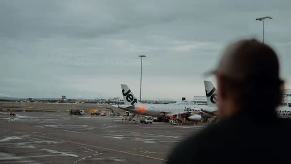 View of Jetstar airplanes parked at Sydney Airport with overcast skies and a passenger silhouette.