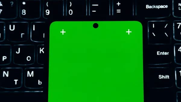 A close-up of a smartphone with a green screen placed on a laptop keyboard.