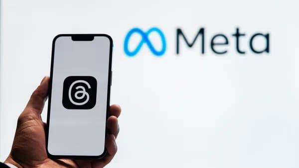 A hand holding a smartphone showing the Threads app with Meta logo in the background.