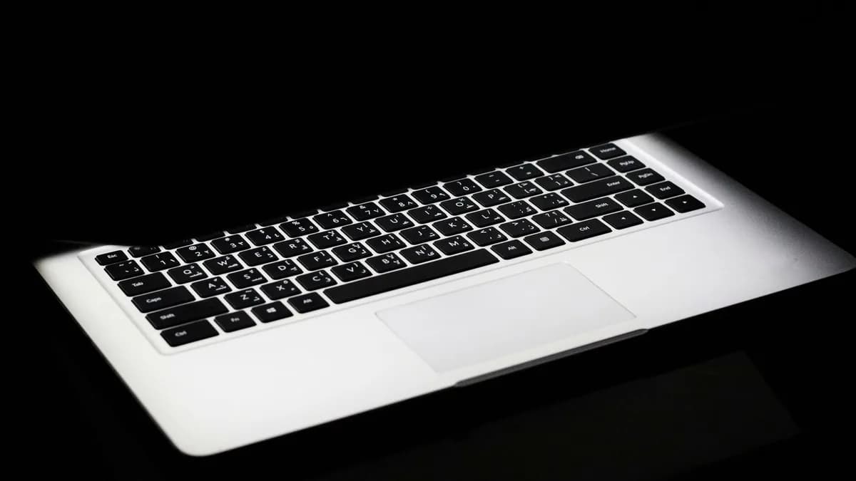 A modern laptop with a glowing keyboard illuminated in a dark, minimalist setting.