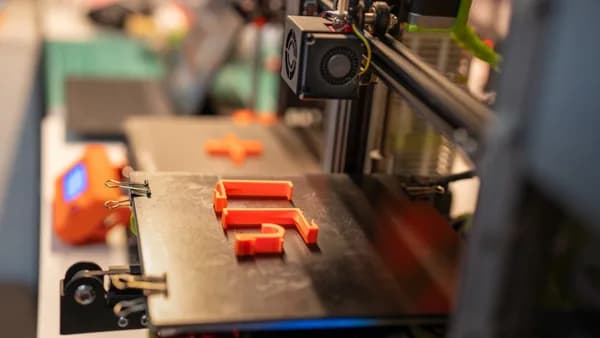 Detailed view of a 3D printer creating an orange plastic part showcasing advanced technology.