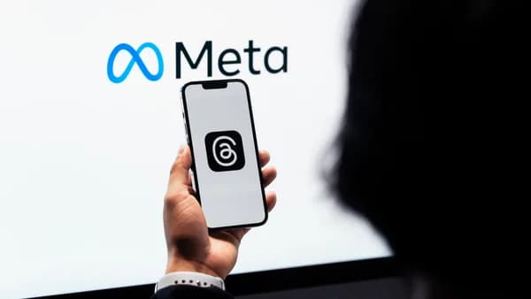 Hands holding smartphone with Meta Threads logo on screen, Meta branding in background.