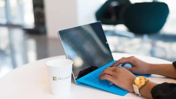 Hands typing on a blue keyboard with a branded cup on a table.