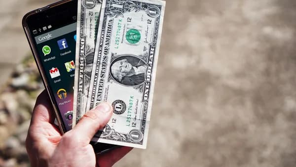 Close-up of a hand holding US dollar bills and a smartphone outdoors, showcasing financial technology.