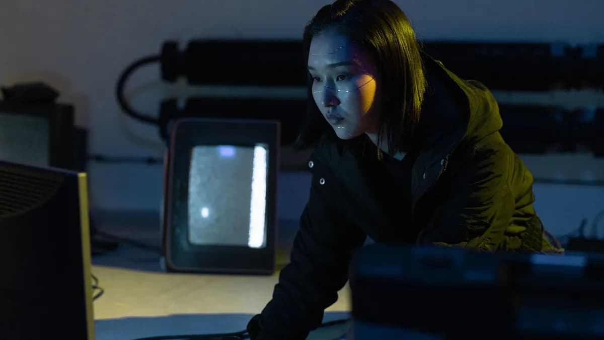 A woman working on a keyboard in a dimly lit room with tech equipment.