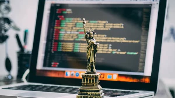 A miniature Statue of Liberty placed on a laptop displaying code, symbolizing freedom in technology.