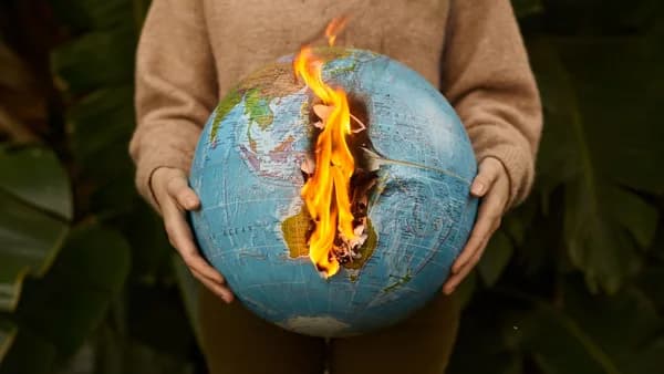 A symbolic portrayal of climate change with a burning globe held in hands, set against a nature background.