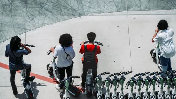 Group of young adults using electric scooters on a sunlit urban pavement.