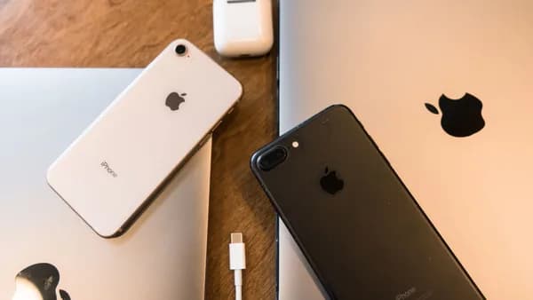 A collection of Apple products including iPhones, MacBooks and AirPods displayed on a wooden table.