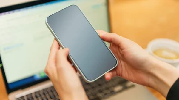 Person holding a smartphone above an open laptop with coffee in the background, ready for work or communication.